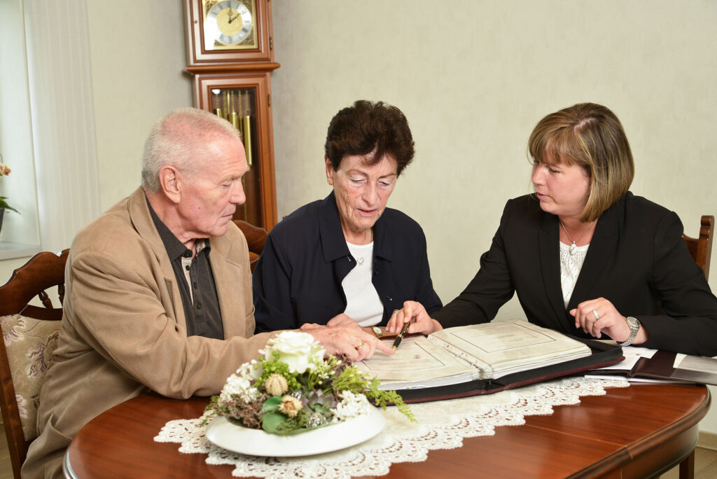 Zwei Mitarbeitende beraten älteren Mann und Frau an einem Tisch.