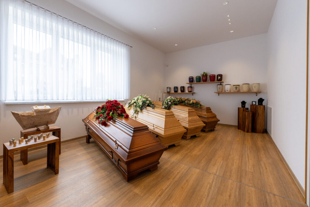 Helles Sarglager mit Särgen auf Holzboden.