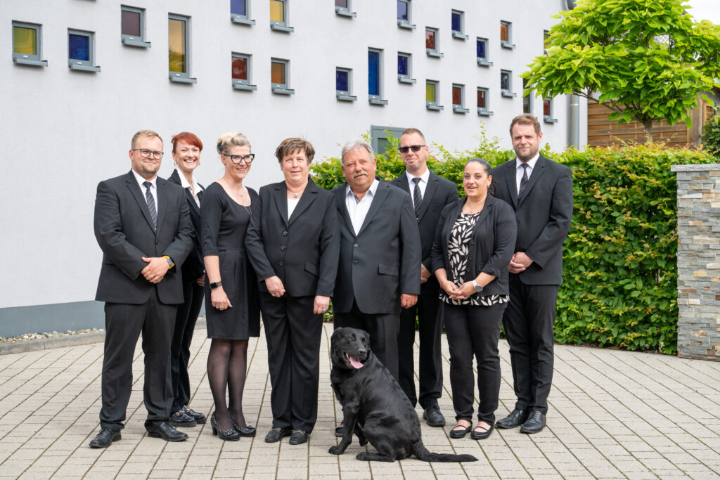 Gruppenfoto des Teams von Bestattungen Lindemann in schwarzer Kleidung mit Hund.