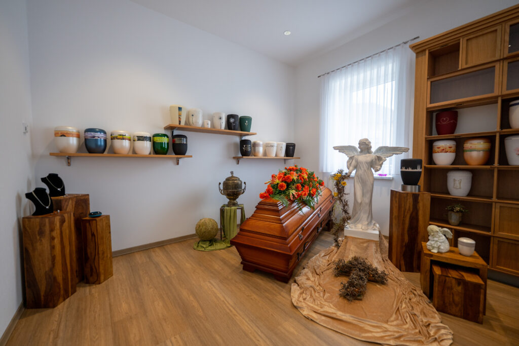 Sarglager Urnenausstellung mit Wandregalen und Blumendekoration.