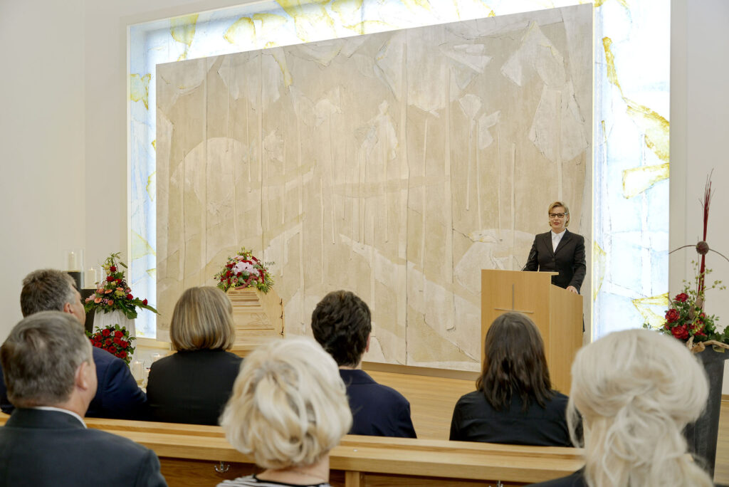 Redner spricht in heller Kapelle vor sitzendem Publikum.