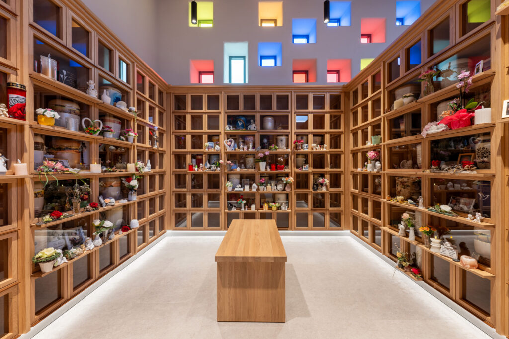 Kolumbarium-Innenraum mit Urnenregalen und bunten Glasfenstern.